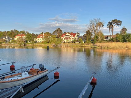 View of a quiet lake surface with a tranquil neighborhood in the background and trees under a blue