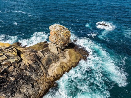 Aerial view of steep granite rocks with a rock tower at Pointe du Raz on the stormy Breton coast,