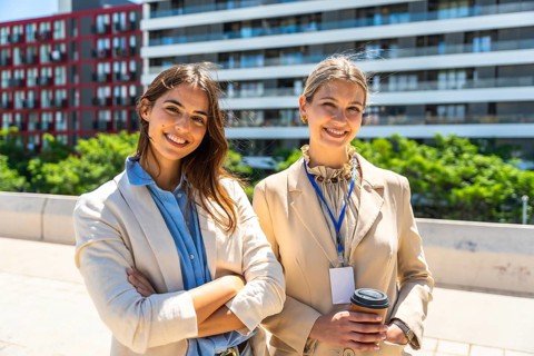 Two cheerful business women, dressed in professional corporate attire, smiling at the camera while
