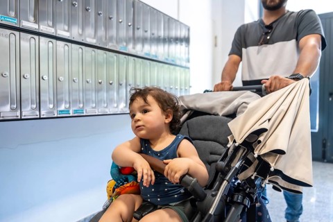 Father pushing a happy toddler in a stroller past a row of metal mailboxes inside an apartment