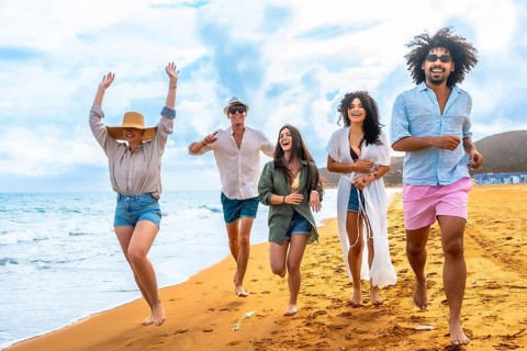 Group of happy multiracial friends enjoying summer vacation, cheerfully running by the ocean