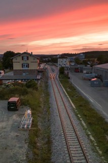 Railway tracks lead through an industrial area at sunset, sky in orange and purple, Hermann Hesse