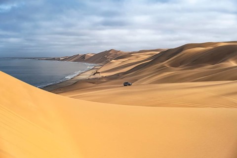 Off-road vehicle drives in dunes, sand dunes and sea in morning light, Atlantic coast and sandy