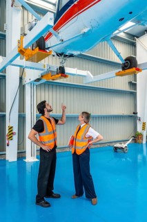 Aviation engineers in safety vests inspect an airplane lifted on service jacks inside a hangar,