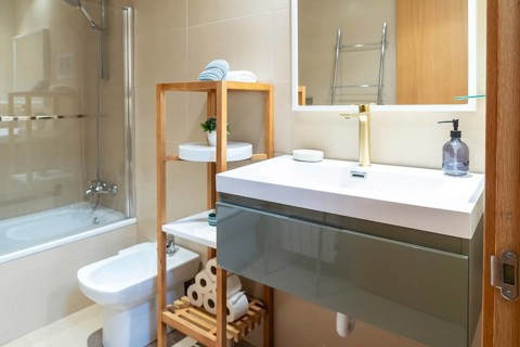 Contemporary bathroom showcasing a white sink with gold faucet, an illuminated mirror, bidet,