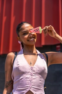 Young woman smiling and holding a watermelon shaped popsicle over her eye, enjoying a refreshing
