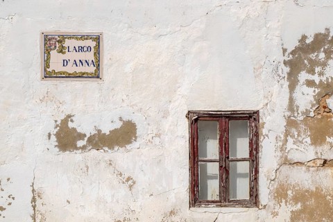 A weathered house façade with an old window and a street sign Largo d' Anna, Tavira, Portugal