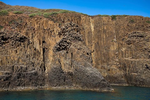 Steep rock wall with basalt columns and sparse vegetation near the sea, Glaronisia, Glaronesia,