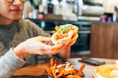 Woman savoring a gourmet bao bun in a modern cafe setting