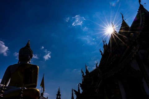 Huge gilded sitting Buddha in backlight, in front of the Wat Phra That Doi Kham Buddhist temple