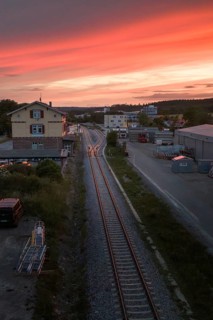 Railway tracks stretch through an industrial park dominated by a colorful sunset, Hermann Hesse