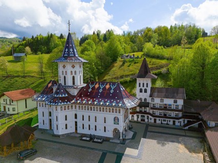 View of an Orthodox church with decorated roof surrounded by green landscape and cloudy sky, aerial