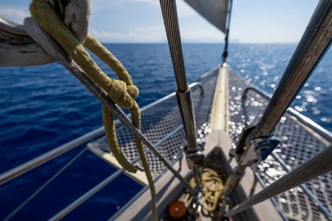 View across the bow of a sailboat to a bright blue sea under a blue sky, Aeolian or Lipari Islands,