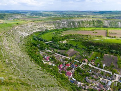 A village surrounded by hills and trees, with an adjacent river course and agricultural land,