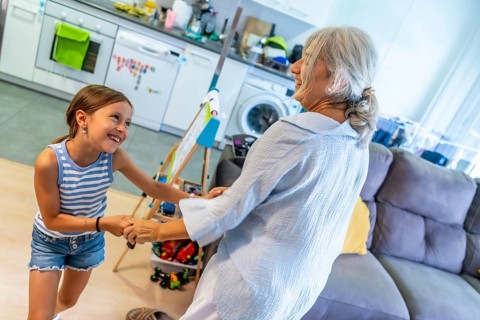 Happy grandmother and granddaughter holding hands and dancing together in a brightly lit home,