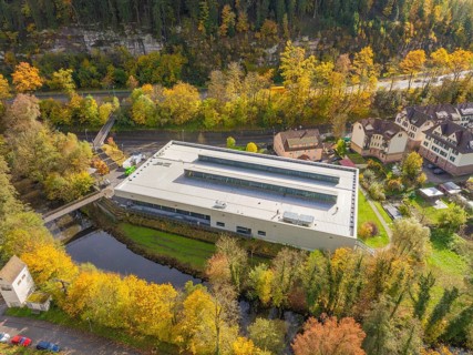 Large industrial building in autumn near a river, surrounded by trees and residential buildings,