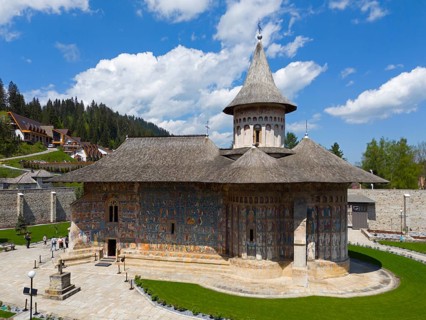 Historic Orthodox church with painted façade, nestled in rural and wooded surroundings under blue