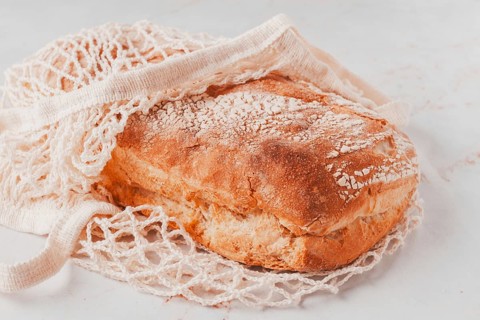 Freshly baked rye bread, ciabatta, in a mesh bag, on a marble light table, natural light