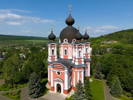 Magnificent orthodox cathedral with black domes surrounded by lush nature and blue sky, aerial