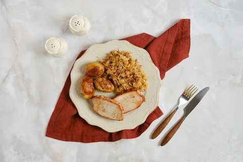 Pork chops with roasted potatoes and sauerkraut on white plate. Meal is placed on red napkin. Salt