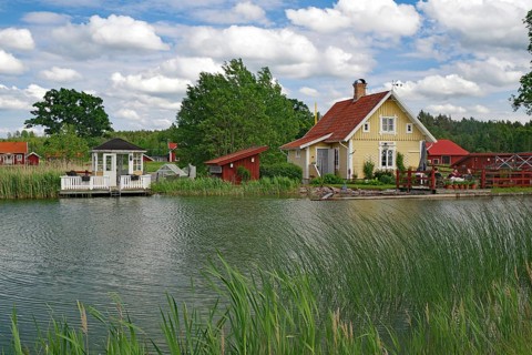 Yellow house with garden on the canal, surrounded by bridges and lush greenery under a blue sky,