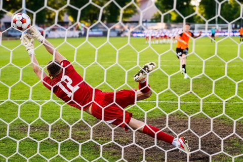 A soccer goalkeeper diving to catch the ball during a dramatic penalty save in a football match in