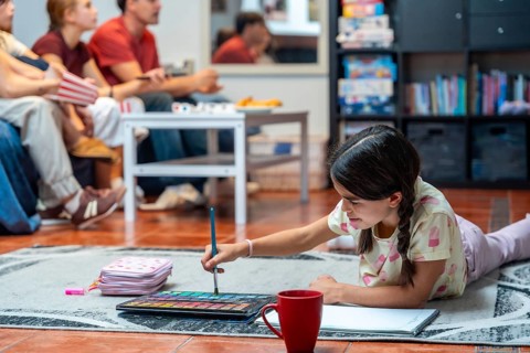 Young girl laying on the floor and engaging in a creative painting activity with watercolors, while
