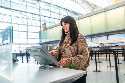 Young woman smiles while using a self service check in kiosk in a bright airport terminal,