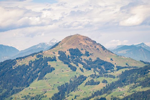 Hilly landscape with green meadows and scattered forests under cloudy sky, Hahnenkamm, Kitzbühel,