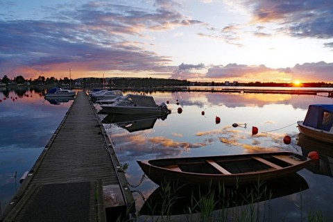 Calm sunset at the harbor with boats and a wooden pier, the water reflecting the colorful sky,