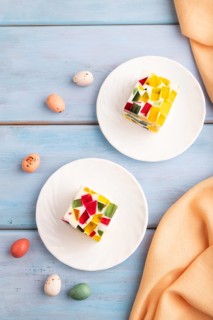 Colored Fruit and milk jelly on blue wooden background and orange linen textile, top view, flat