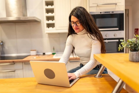 Young woman wearing glasses and a turtleneck shirt concentrating on her laptop while sitting at a