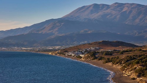 Komos Beach, coastal landscape with mountains in the background and a small settlement along the