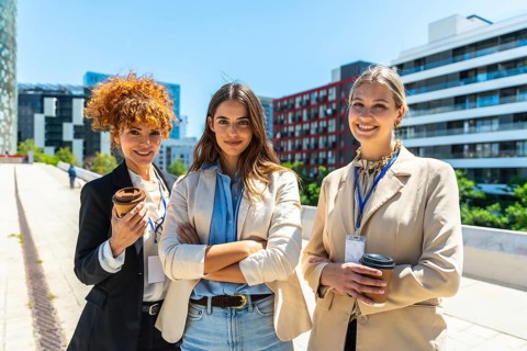 Three confident businesswomen standing together and smiling in a modern city setting, representing
