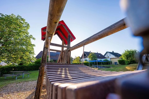Wooden structure of a playground with a view of a clear blue sky and houses in the background,
