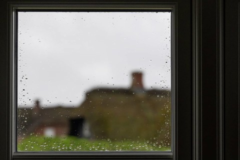 View through a window pane with raindrops beading, blurred traditional thatched Danish houses in