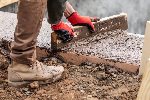 Construction Worker Leveling Wet Cement Into Wood Framing
