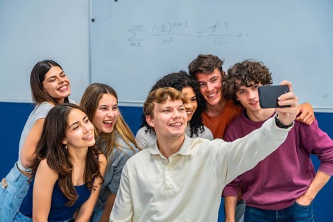 Group of young diverse students in a classroom smiling and laughing while taking a selfie together