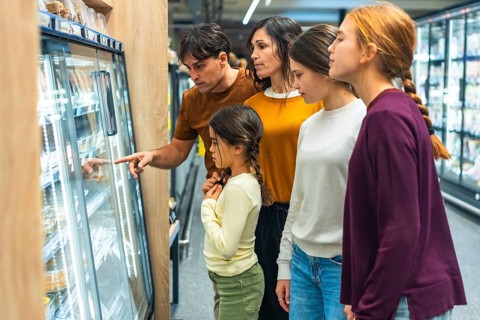 Family group of mother, father, and three daughters standing next to a refrigerated display in a