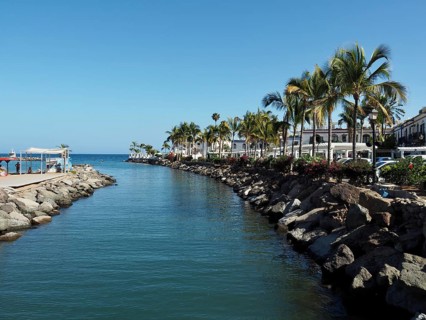 A quiet water channel lined with palm trees and rocks overlooking the sea, Puerto de Mogan, Gran