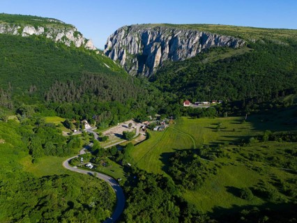 A small village nestled in a green valley flanked by impressive rock faces, aerial view, Cheile