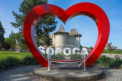Large red heart sculpture with SOROCA lettering and castle in the background in a park, Soroca
