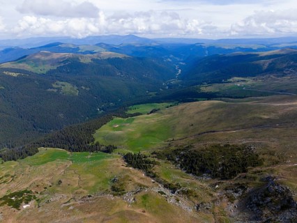 View of a wide valley with forests and mountains on the horizon under blue sky, aerial view,