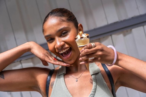 Young woman with radiant skin smiling brightly, holding a delicious ice cream cone with chocolate