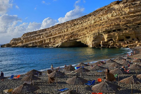 Neolithic caves, former hippie paradise, visited beach with colorful umbrellas against huge cliffs