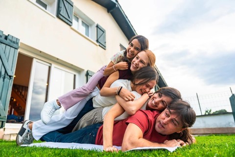 Smiling multi ethnic family members piling on top of dad in a playful human pyramid on green grass,