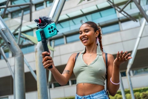 Young woman recording content with her smartphone and a microphone, creating a video for social