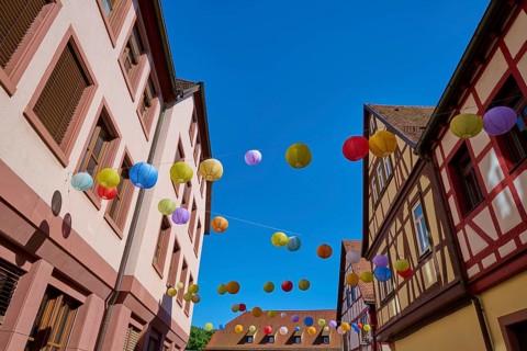 Colourful lanterns hang over a street with half-timbered houses on a sunny day, Lohr am Main,