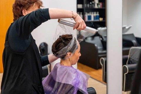 Hairdresser applying plastic wrap over a client's hair after a coloring treatment, working inside a