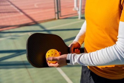 Player prepares to serve during a pickleball game, holding a black carbon paddle and bright yellow